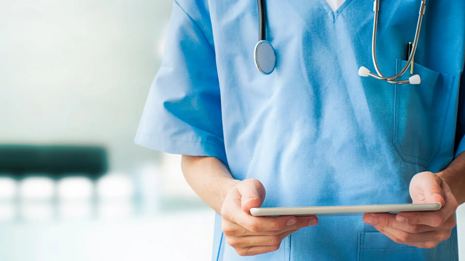 Close up of a doctor in blue scrubs with a stethoscope around their neck holding a health chart.
